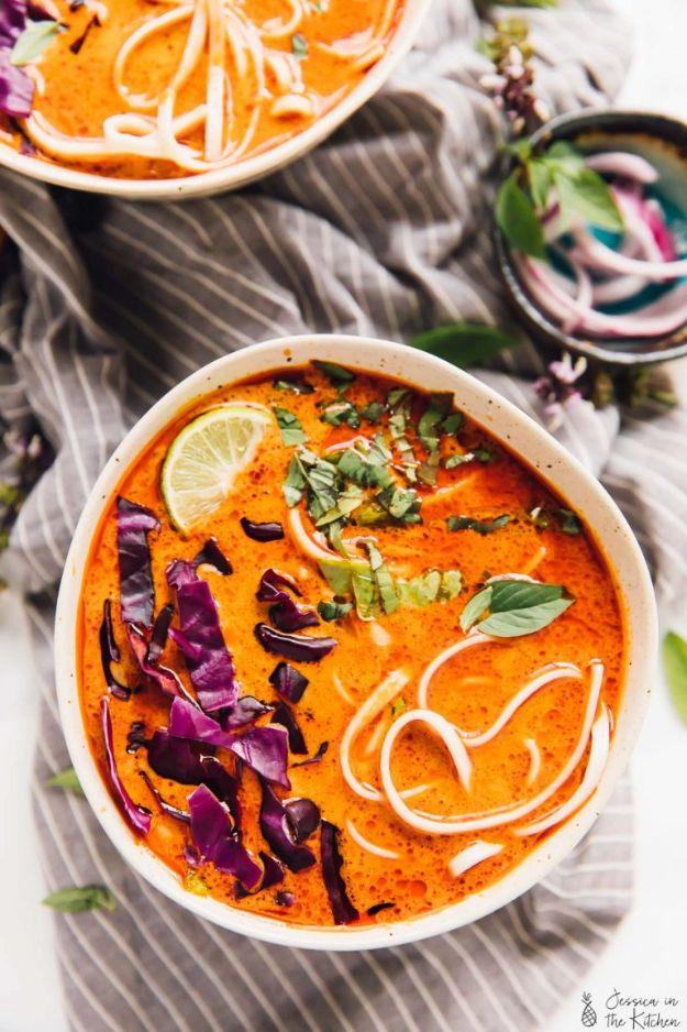 Two bowls of vegan coconut curry noodle soup topped with purple cabbage, fresh herbs and a lime wedge