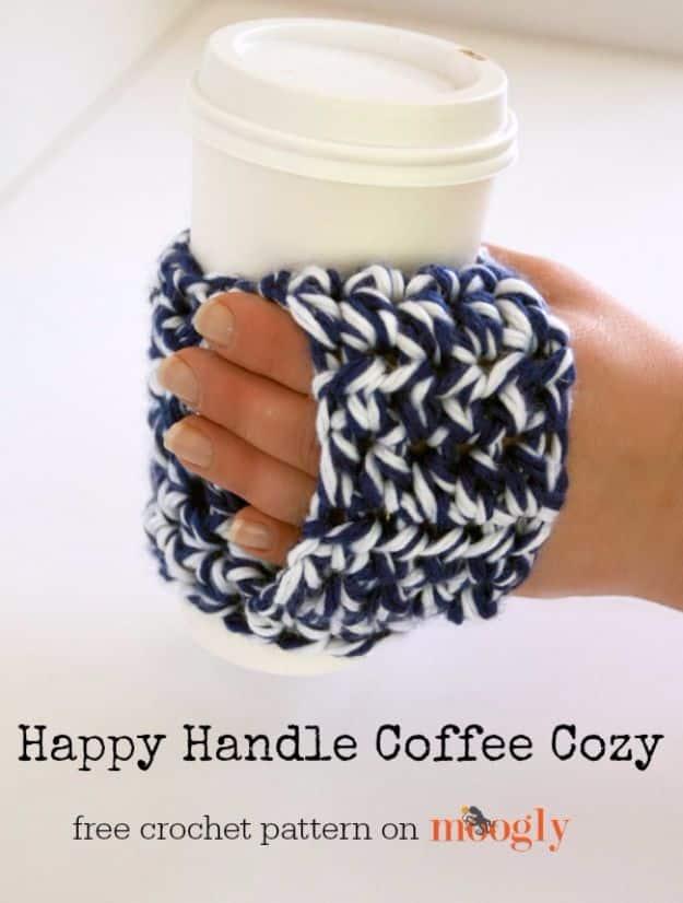 Happy handle coffee cozy, a hand holding a white to go cup wrapped in a navy and white crochet cozy with a handle