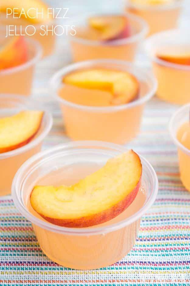 Peach fizz jello shots in lidded two ounce cups, each topped with a thin slice of fresh yellow peach