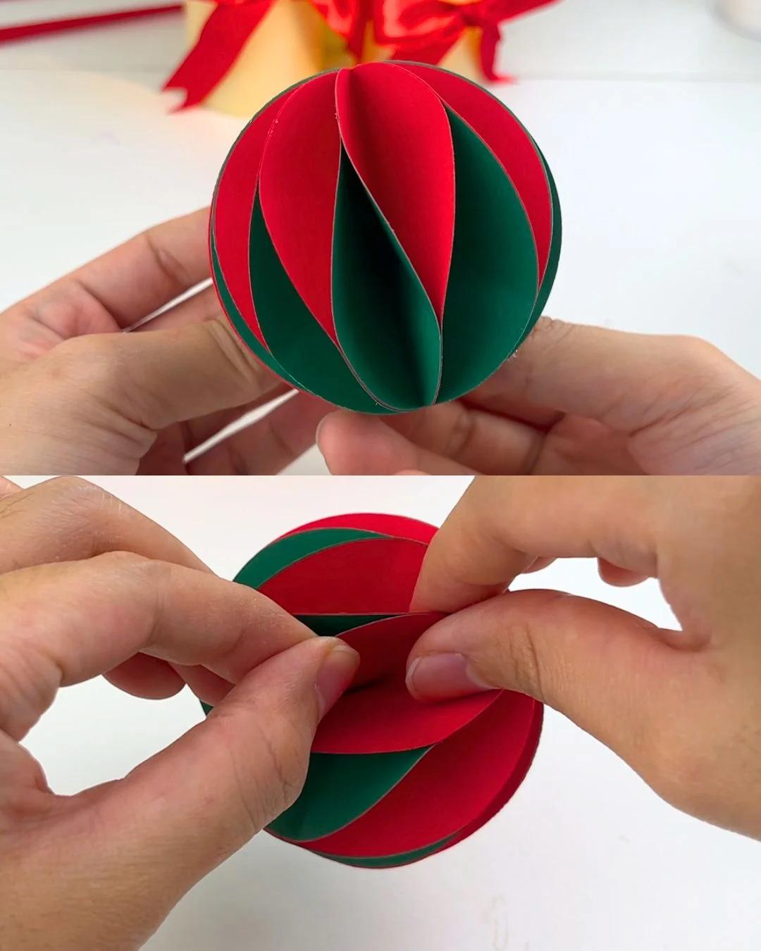 Best DIY - two hands holding a nearly finished red and dark green striped paper ball and pressing the last two ends together