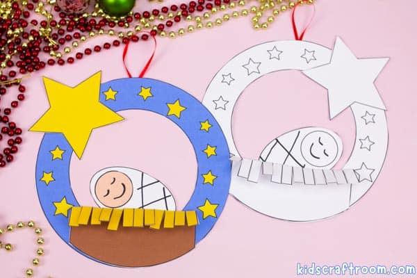 Two paper Baby Jesus wreath crafts, one colored blue with a yellow star and brown manger and one black and white to color