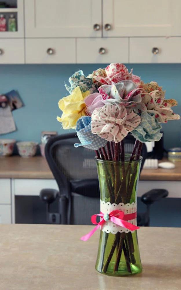 Quilting scraps fabric roses in pink blue and yellow prints on bare twig stems in a green glass vase