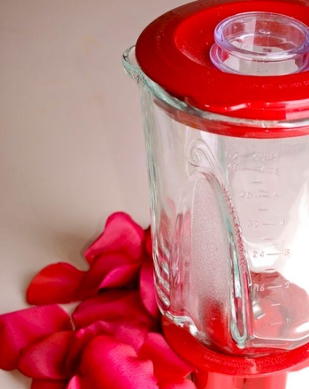 Rose petal beads, a glass blender jar with a red lid standing on a white surface surrounded by loose bright pink rose petals