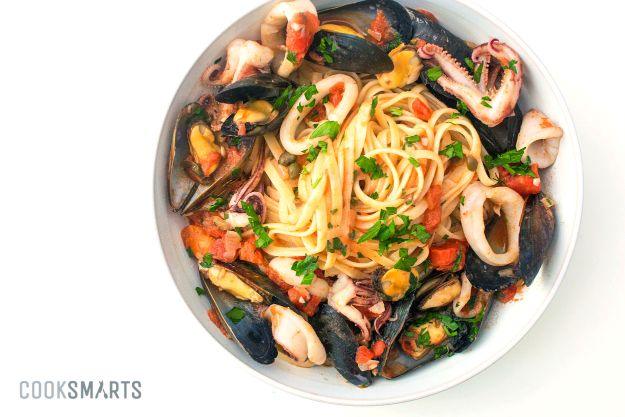 Italian seafood pasta with mussels and calamari, linguine in a white bowl with open mussel shells and squid rings