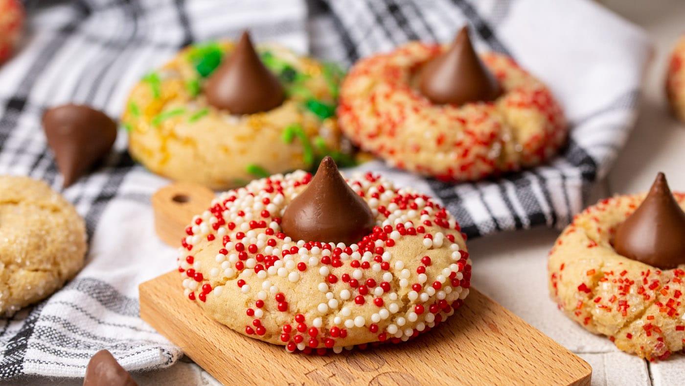 Peanut butter blossom cookies rolled in red, white and green sprinkles with a chocolate kiss pressed in the center of each