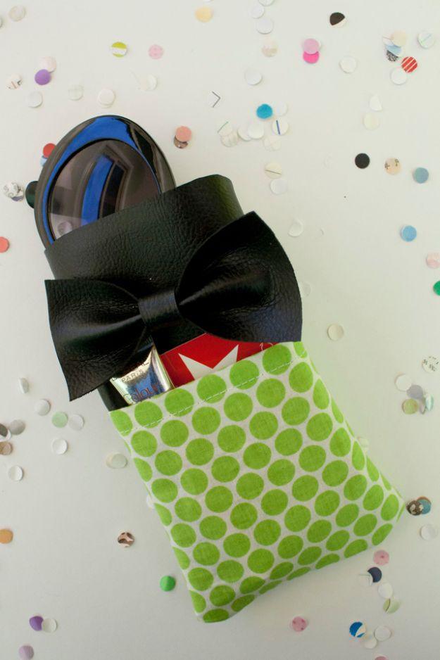 Green polka dot sunglasses case with a front pocket and a black faux leather bow, lying on a white confetti surface