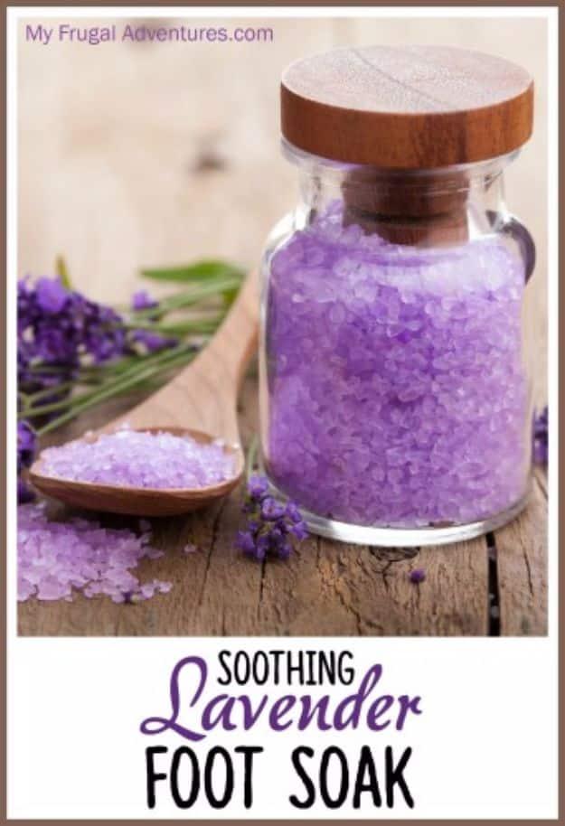 Glass jar with a wooden lid filled with purple lavender foot soak salts beside a spoon and fresh lavender