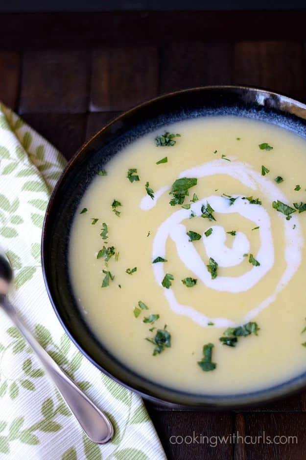 Irish potato leek soup in a dark blue bowl with a swirl of cream and chopped parsley, spoon beside it