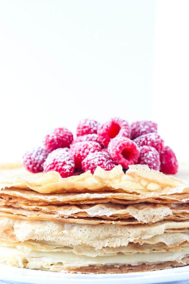 Tall stack of thin coconut oil crepes layered with whipped cream and topped with fresh red raspberries
