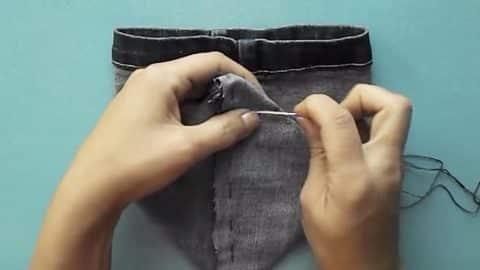 Recycled bag from jeans, two hands stitching a dark denim waistband with black thread against a teal background