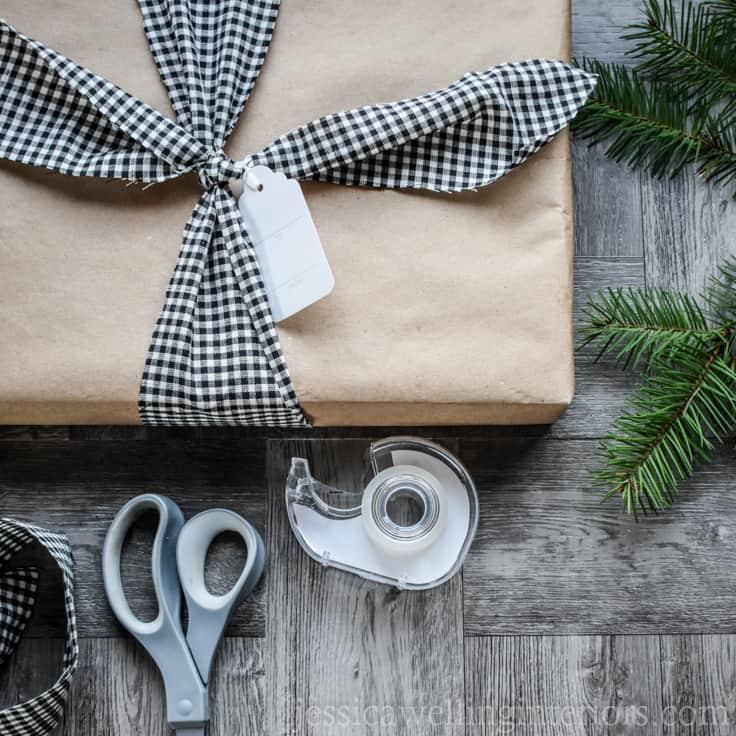 A kraft paper parcel tied with black and white check fabric strips and a blank tag, beside scissors and tape