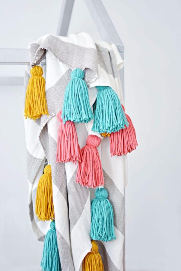Gray and white geometric throw hung on a wooden rail, edged with fat yarn tassels in mustard, coral and teal