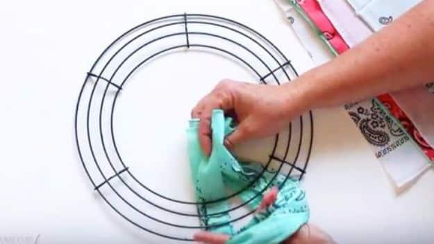 Hands tying a strip of turquoise bandana fabric onto a black wire wreath form during a wreath tutorial