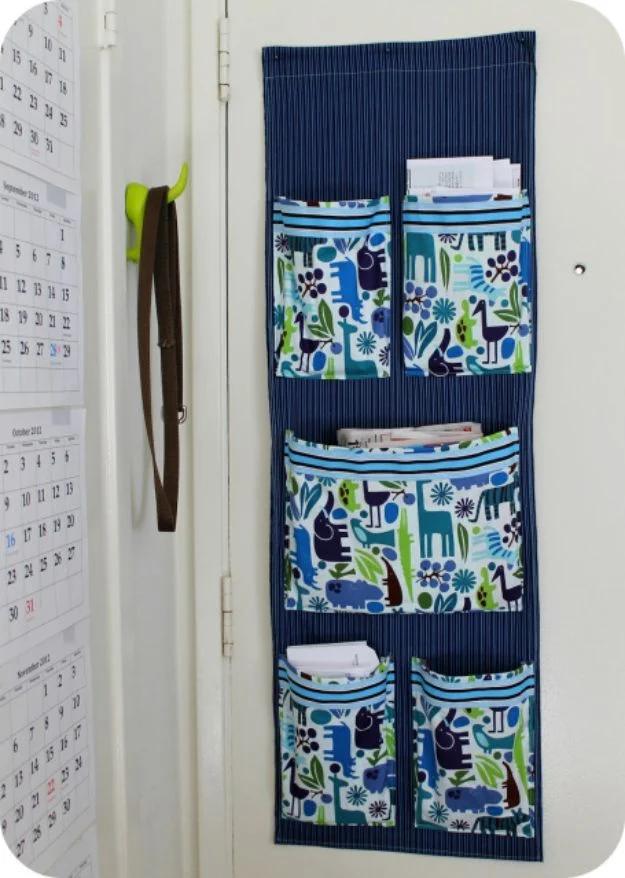 Navy fabric wall organizer on a door with five patterned pockets holding mail, beside a printed wall calendar