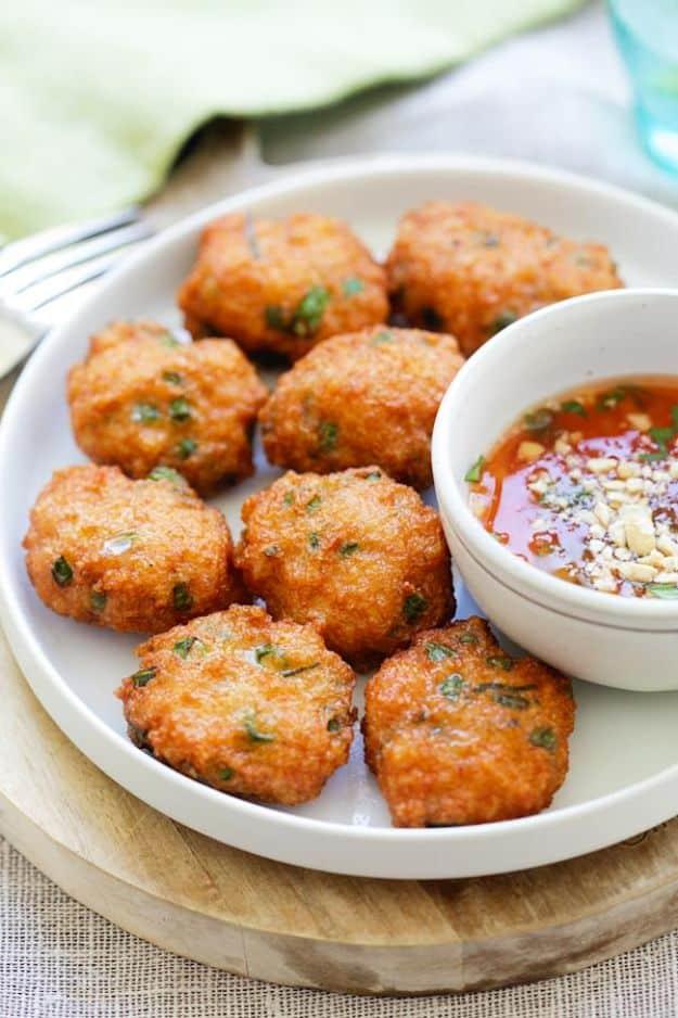Thai shrimp cakes, golden fried patties on a white plate with a small bowl of sweet chili dipping sauce