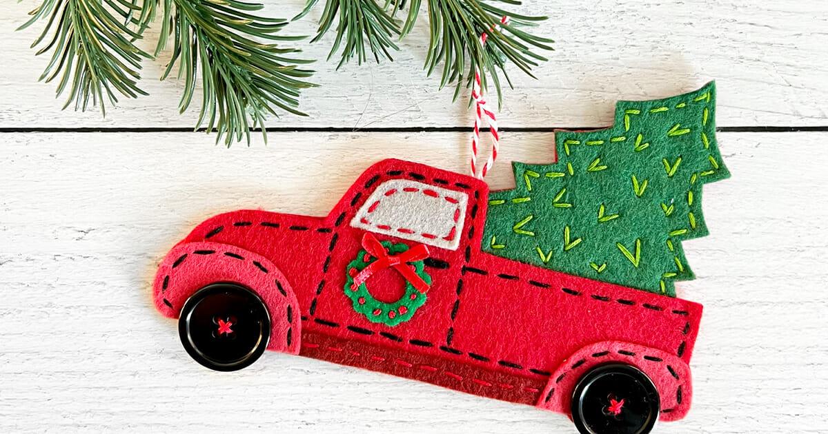 A red felt vintage truck ornament with a stitched green tree in the bed, button wheels and a tiny wreath on the door