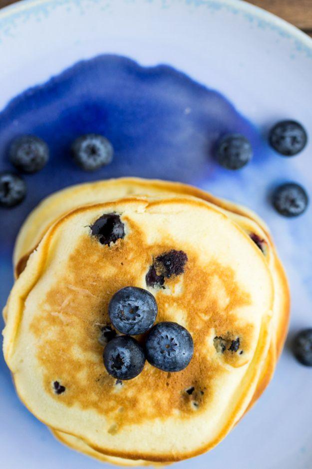 Fluffy blueberry pancakes on a blue and white glazed plate with fresh blueberries pressed into the top pancake