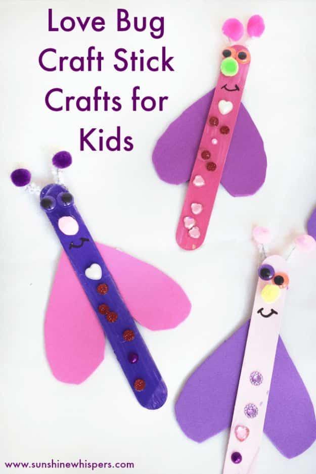 Two craft stick love bugs with purple and pink foam heart wings, pom pom antennae and stuck on jewel decorations