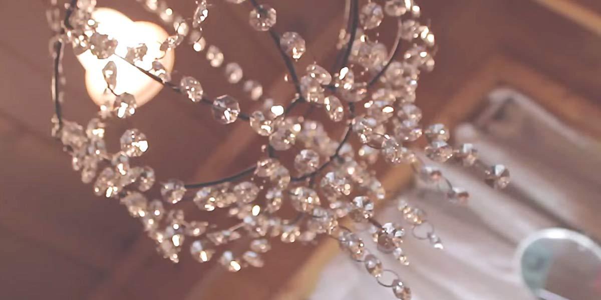 Close up of a beaded chandelier made from a wire plant basket hung with clear crystal bead strands and a lit bulb