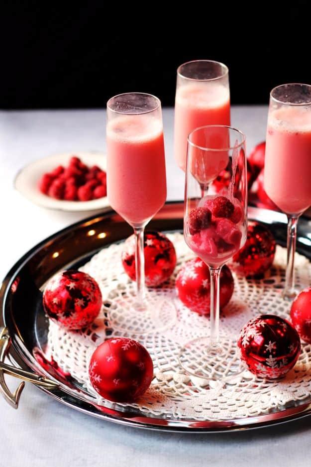 Pink raspberry cream mimosas in champagne flutes on a silver tray with red ornaments and fresh raspberries