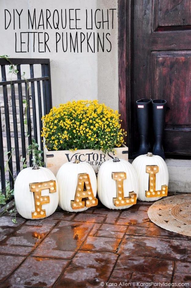 Four white pumpkins on a wet brick porch spelling out FALL in gold marquee letters lit up from inside