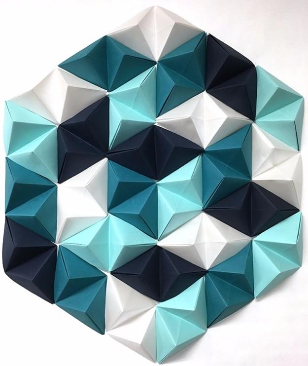 DIY geometric paper wall art, a large hexagon of folded paper pyramids in white, aqua, teal and navy on a pale wall