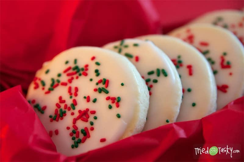 Round glazed sugar cookies with white almond icing and red and green sprinkles nestled in red tissue paper