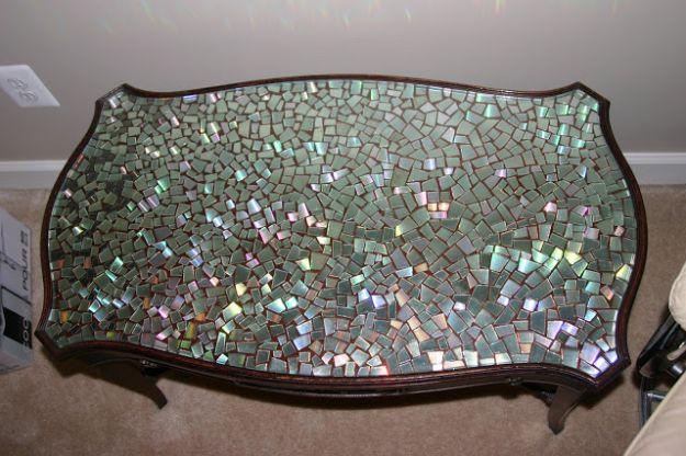 Dark wood side table with a shaped top filled edge to edge with a mosaic of small iridescent CD tiles under a glass overlay