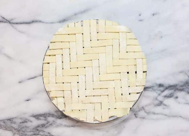Unbaked pie crust topped with a herringbone lattice of short pastry strips in alternating blocks on marble