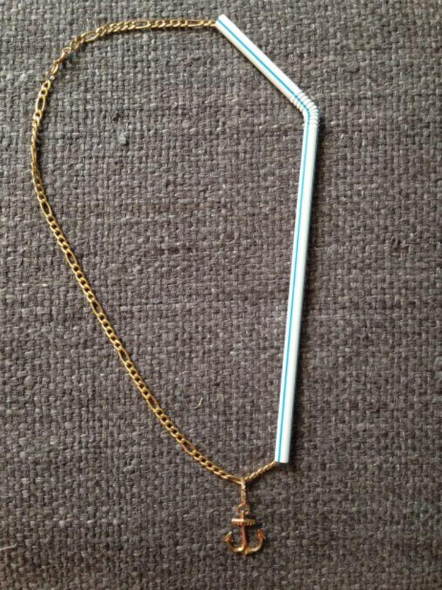 Gold chain necklace with a small anchor charm threaded through a clear drinking straw on burlap fabric