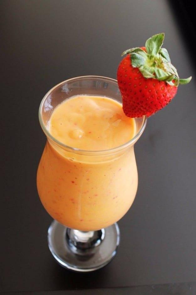 Orange pink strawberry mango smoothie in a footed hurricane glass with a whole strawberry perched on the rim