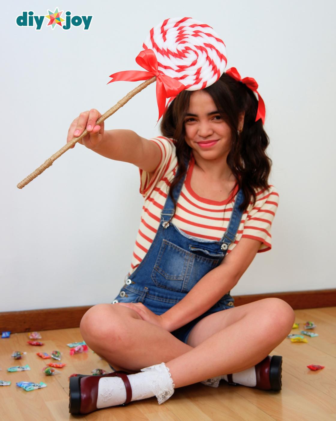 DIY Ideas for Halloween - a young woman sitting on a wood floor, holding up the giant swirl lollipop prop