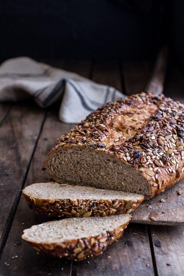 Dark seeded whole grain loaf sliced on rustic wood with a grey cloth, seeds visible across the crust