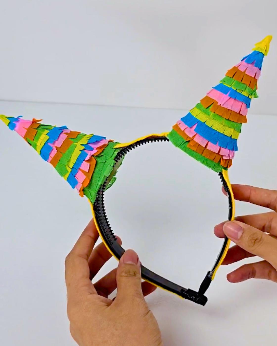 DIY Costume Accessories - a black headband held in two hands with two fringed cone horns covered in layered crepe paper