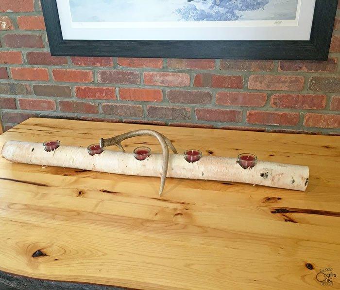 Long birch log centerpiece with glass tea light holders set into drilled holes and an antler laid across it
