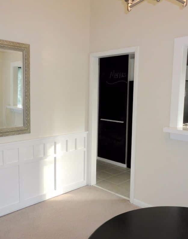 White painted door trim and skirting boards framing a doorway with a black chalkboard door and white board and batten