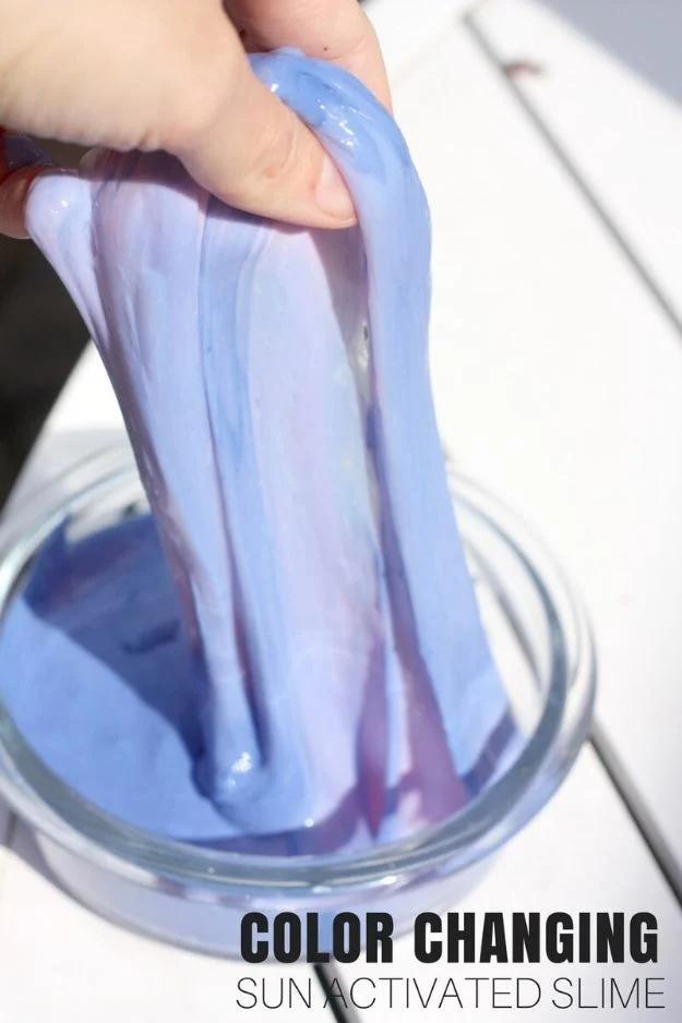 Purple color changing slime being stretched out of a glass bowl by a hand, made with sun activated pigment