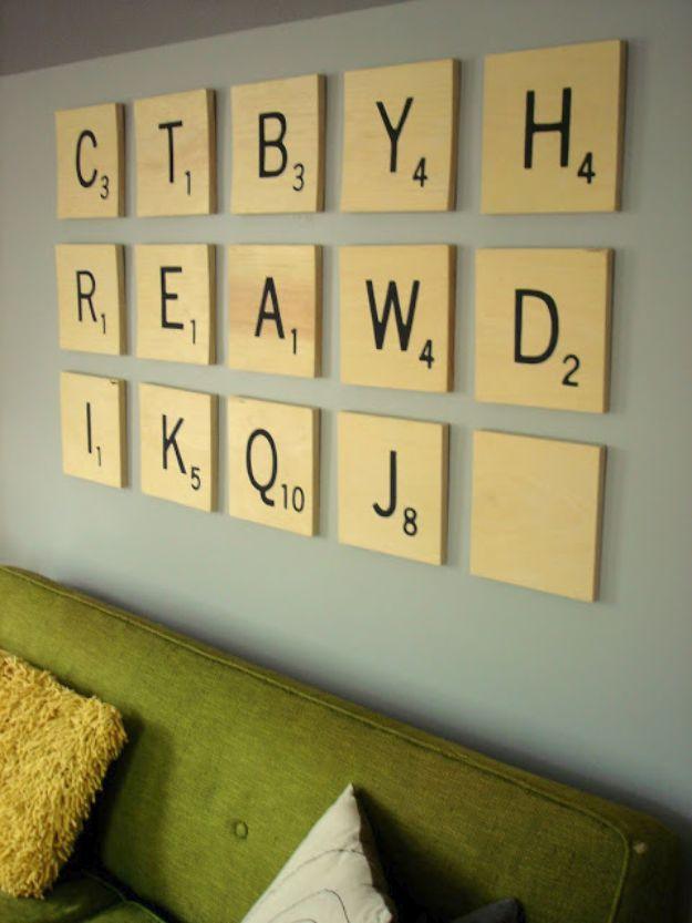 Oversized painted wooden Scrabble letter tiles hung in rows on a pale wall above a green upholstered bench
