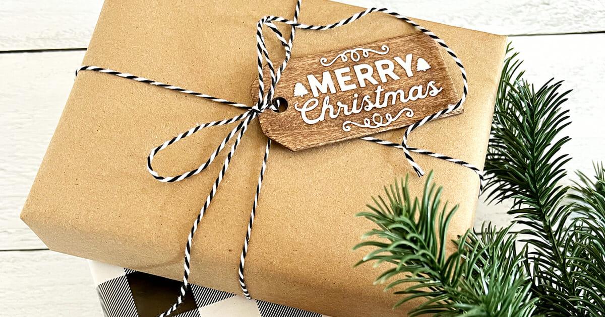 A kraft paper parcel tied with black and white twine and a small stained wood tag reading Merry Christmas