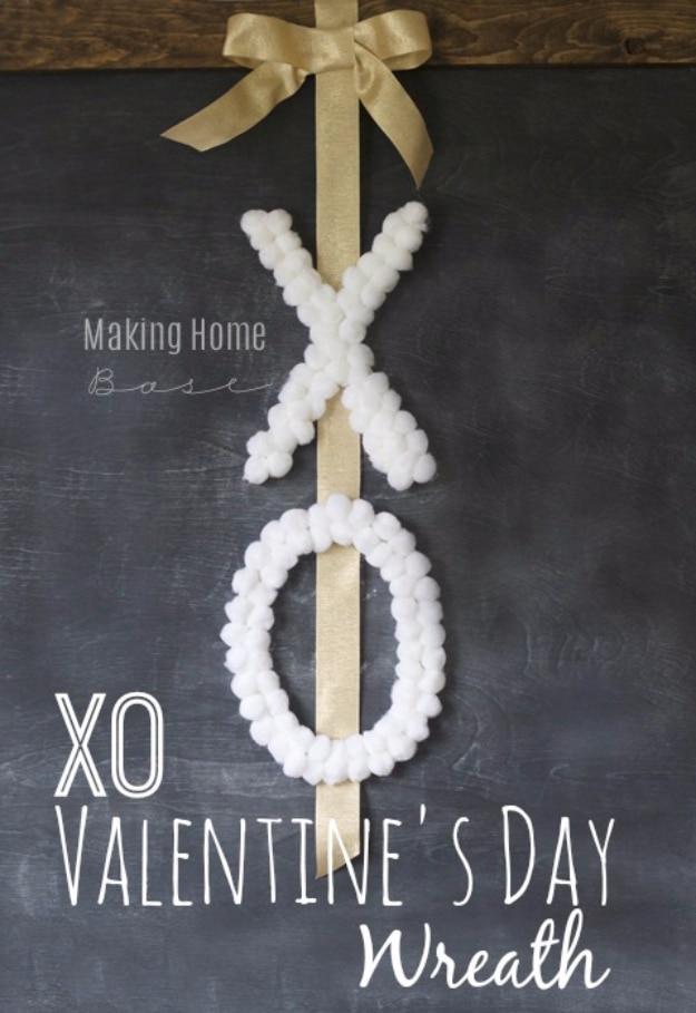 XO wreath made from a yarn wrapped letter X and a painted letter O hanging on a white front door in pink and red