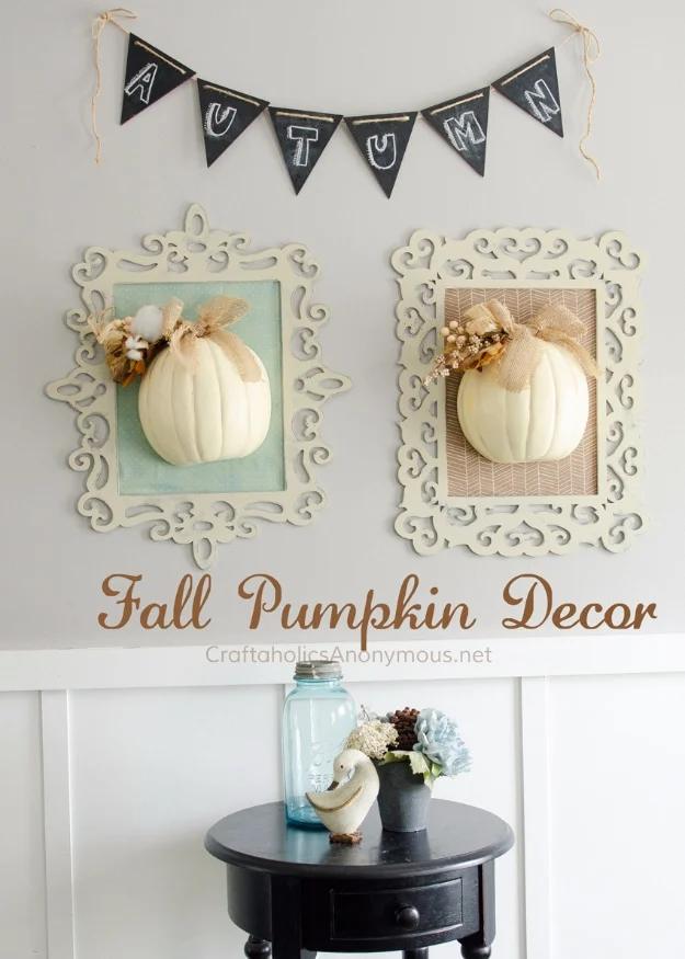 Distressed cream wood frame backed with fall fabric holding two white half pumpkins with burlap bows