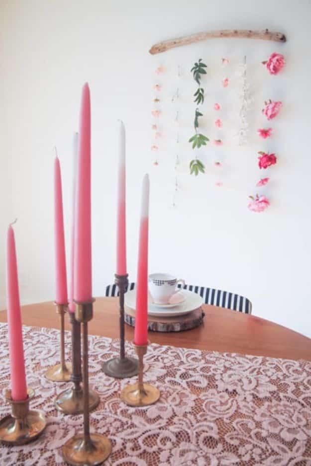 Faux flower wall hanging strung from driftwood above a table with pink taper candles, a beginner decor idea