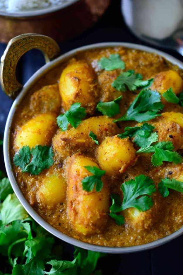Metal karahi pan of baby potatoes in a thick orange curry sauce topped with fresh green cilantro leaves