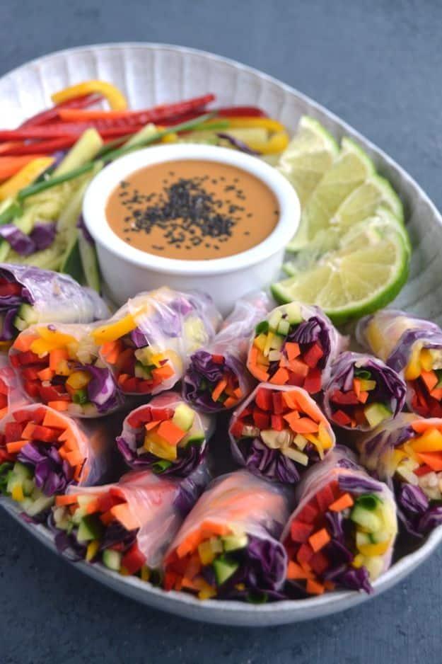 Rainbow veggie spring rolls cut in half in a bowl showing pepper, cabbage and carrot, with peanut dipping sauce