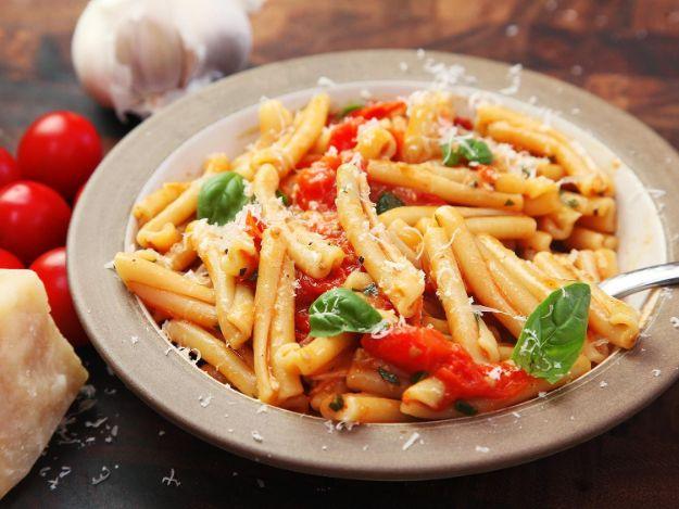 Pasta with blistered cherry tomato sauce in a grey bowl, tossed with fresh basil and plenty of grated parmesan