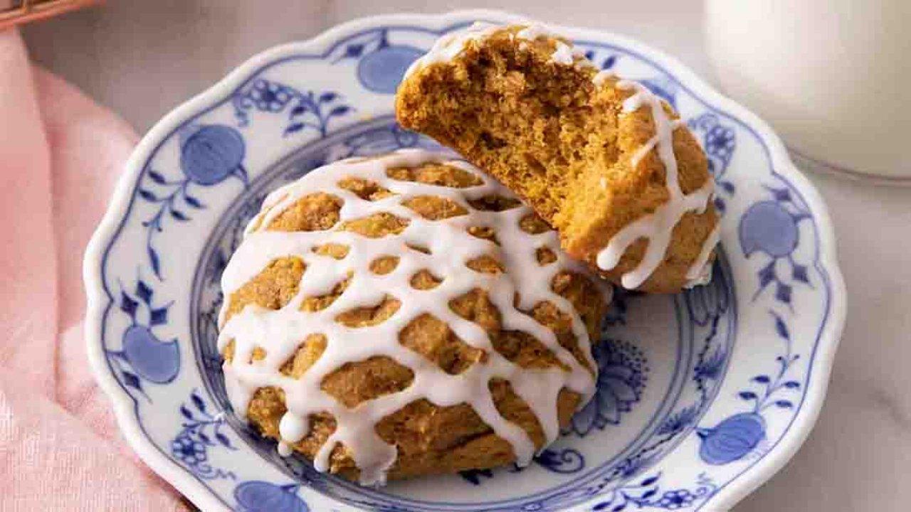 Glazed soft pumpkin cookies on a blue and white china plate, one broken open to show the soft cakey crumb
