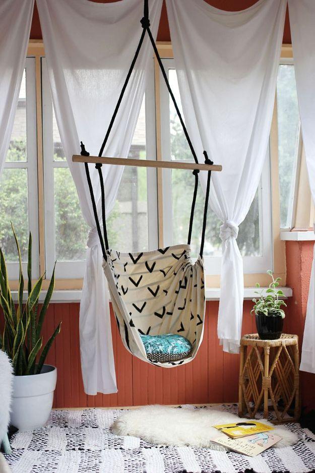 Hammock chair in cream canvas with a black arrow print, hung from a wooden dowel in a porch with white curtains