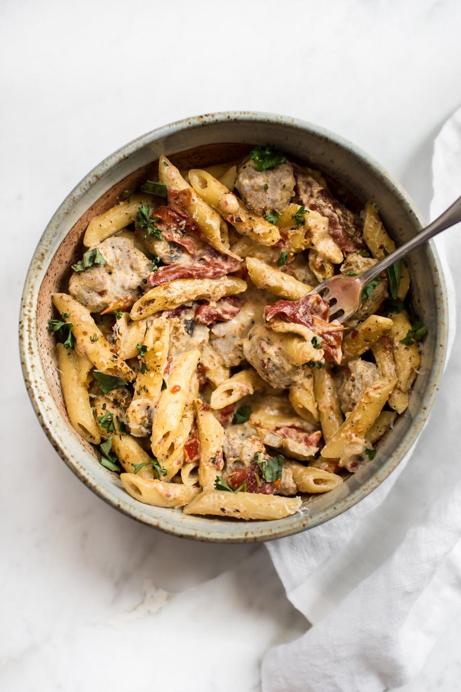 One pot Cajun sausage pasta, creamy penne with browned sausage pieces and sun dried tomatoes in a stoneware bowl