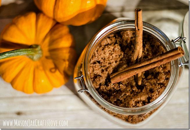 Open clamp lid glass jar packed with brown spiced sugar scrub and cinnamon sticks beside small orange pumpkins