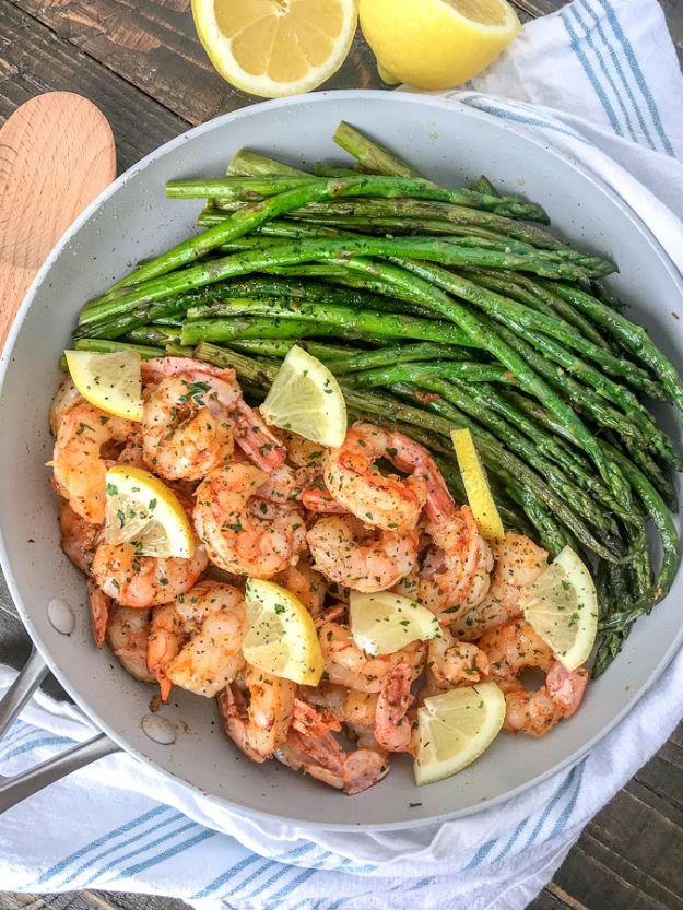 Lemon garlic butter shrimp with asparagus in a silver skillet, pink shrimp and green spears with lemon wedges